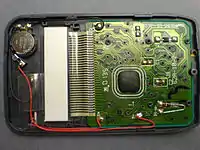 The interior of a newer (c. 2000) pocket calculator. It uses a button battery in combination with a solar cell. The processor is a "Chip on Board" type, covered with dark epoxy.